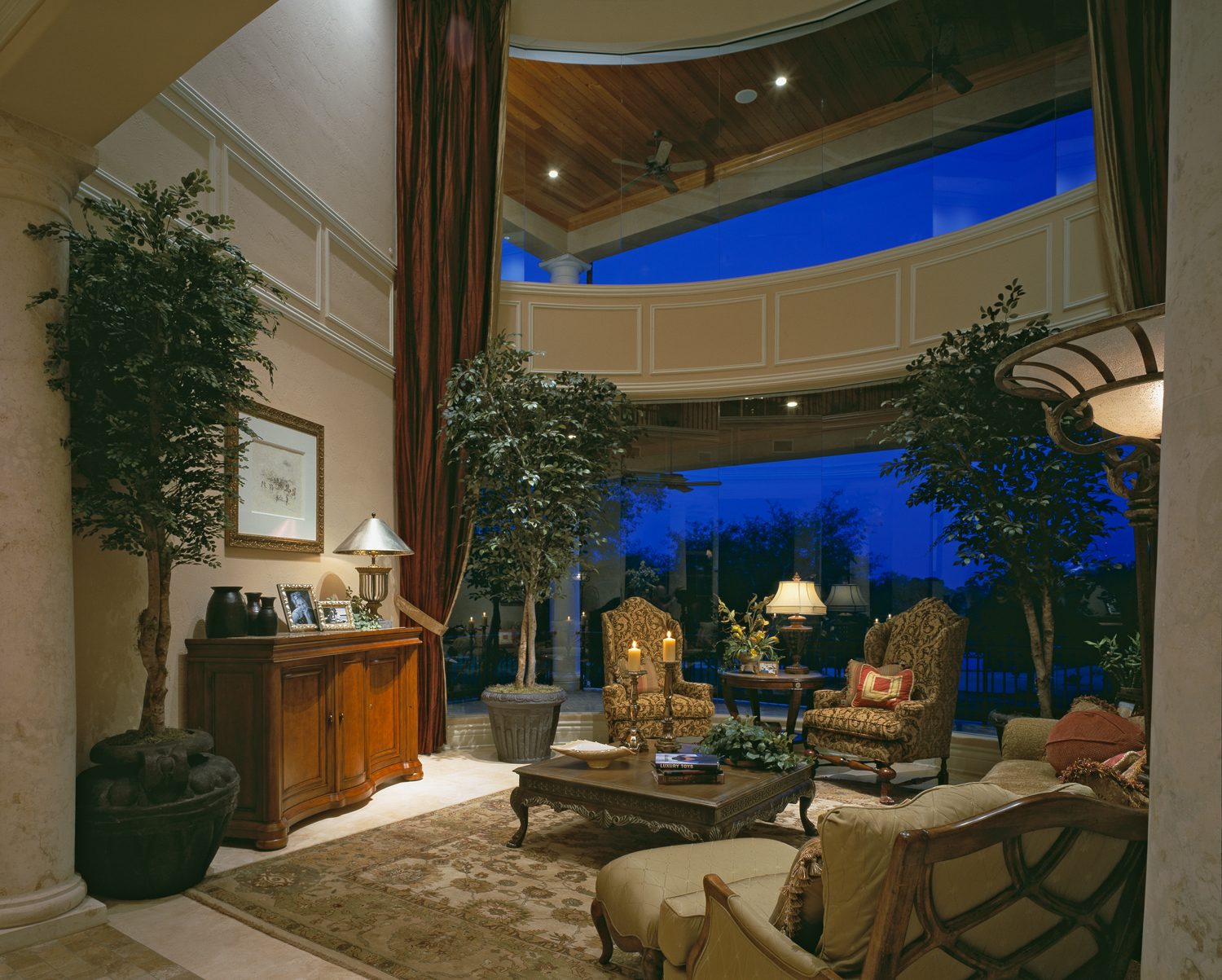 Two-story living room with tall windows, draperies and a balcony overlooking the evening sky