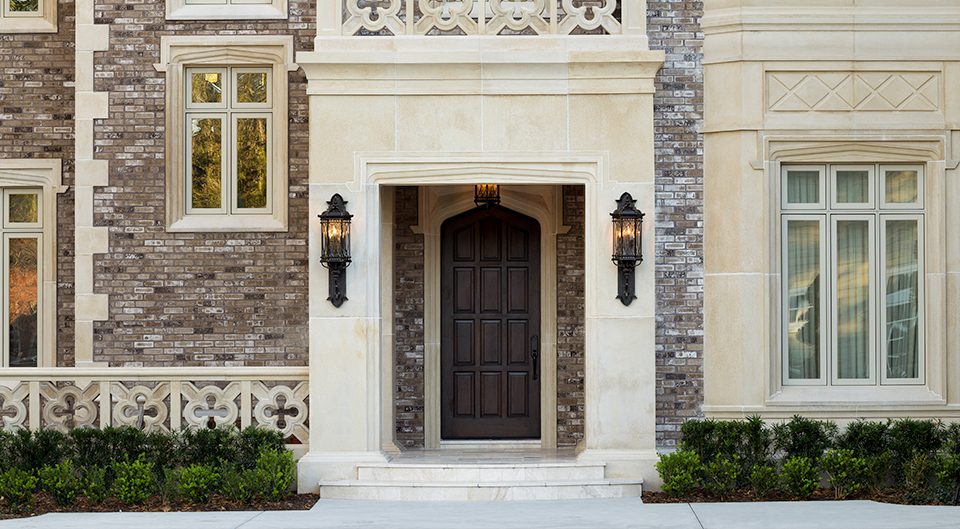 Limestone and brick home entry with an arched wood door flanked by lanterns