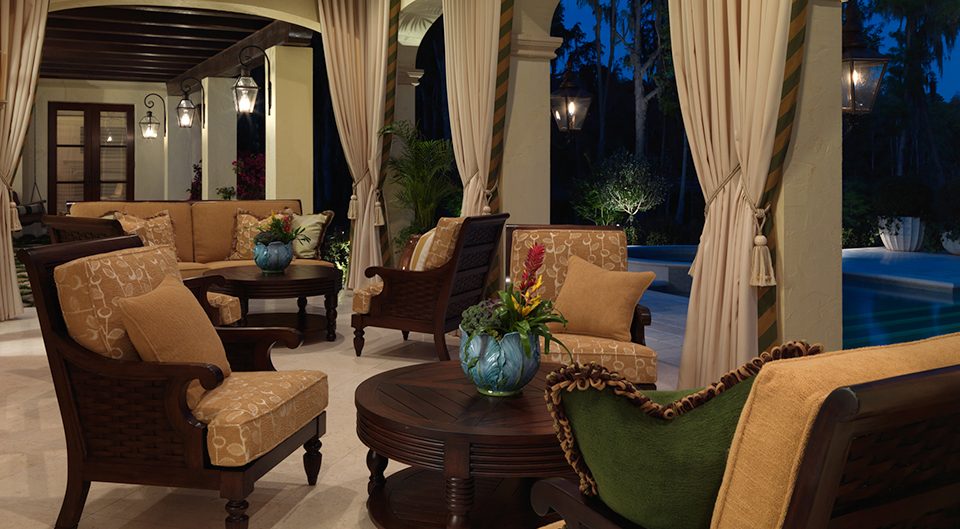 Covered patio seating with drapes and lanterns beside a pool at night