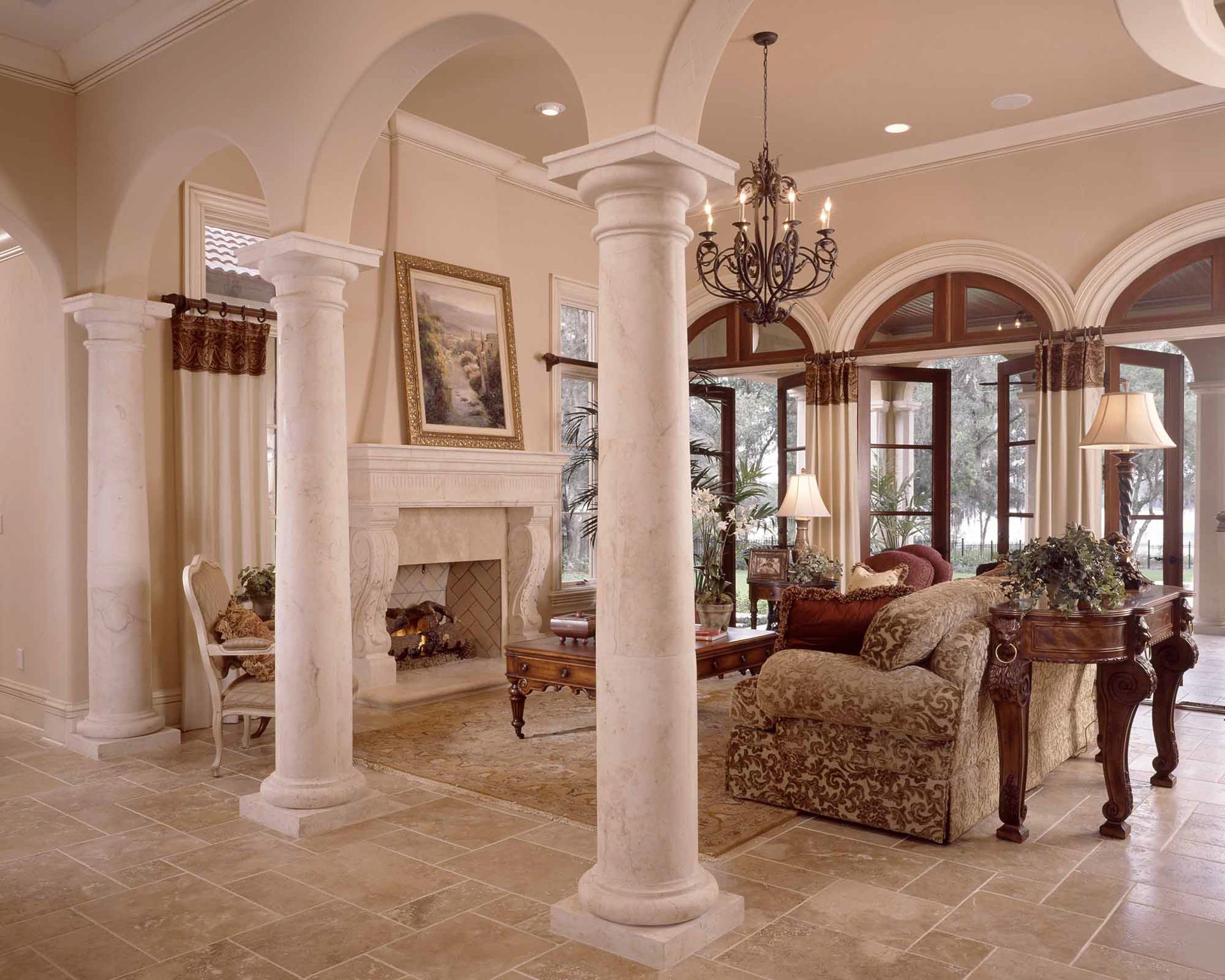 Living room with stone columns, arched French doors, a carved fireplace and a wrought-iron chandelier