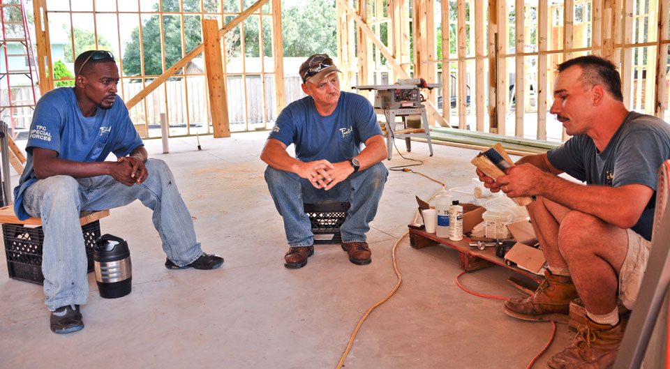 Three Fechtel crew members talking inside a wood-framed home under construction