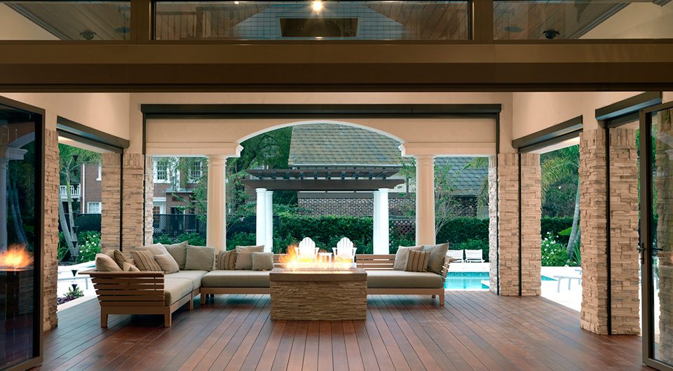 Covered outdoor living room with a fire table, stacked-stone columns and a pool beyond